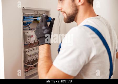 Electrical technician in uniform installing and connecting electrical equipment in a switchboard with fuses Stock Photo