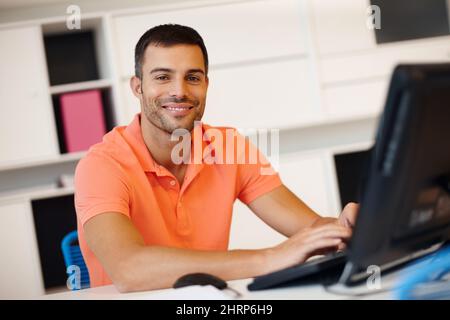 He enjoys his work. A smiling young entrepreneur working at his computer. Stock Photo