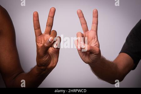 Close up of two hands, african and caucasian, making the Victory sign, concept of integration, diversity and multi ethnicity Stock Photo