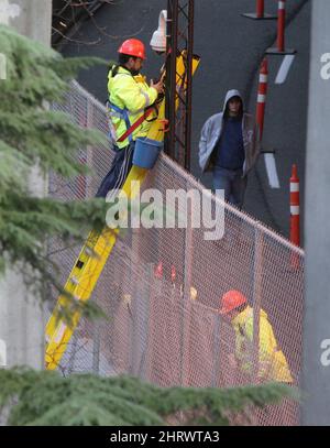 A pedestrian walks past workers installing a security cameras on a temporary fencing barrier outside B.C. Place Stadium, the site of opening ceremonies for the Vancouver 2010 Winter Olympic Games, in Vancouver, B.C., on Wednesday January 6, 2010. Security barriers and cameras have begun to go up in downtown Vancouver in preparation for the games. THE CANADIAN PRESS/Darryl Dyck Stock Photo