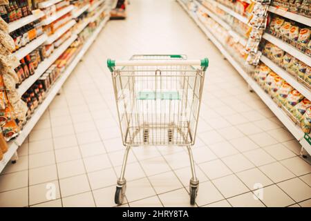 Empty shopping cart with abstract blur supermarket discount store aisle and product shelves interior defocused background Stock Photo