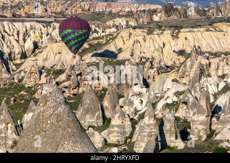 A hot air balloon floats above volcanic rock formations known as fairy chimneys in Love Valley at Goreme in the Cappadocia region of Turkey. Stock Photo