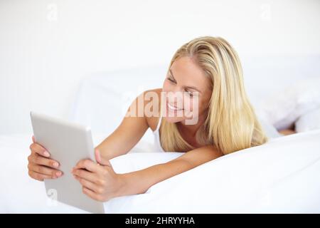Browsing in comfort. A beautiful young blonde woman working on her digital touchpad while lying in bed. Stock Photo
