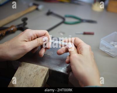 an unrecognizable adult worker woman working in her jewelry artisan workshop holding a piece of metal with an inscription in spanish Stock Photo