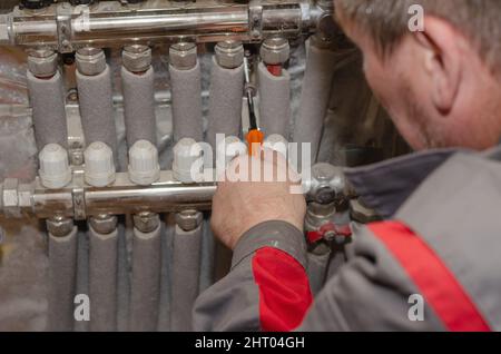 Repair and maintenance of heating systems concept. Specialist makes repairs to your floor heating system. Adult male adjusts valves on water manifold. Stock Photo