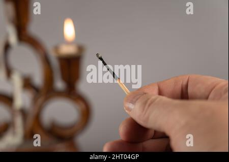 A man's hand holds an extinguished match against the burning candles. Brown ceramic candlestick in the background. Gray background. Closeup. Selective Stock Photo