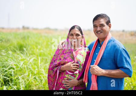 Portrait shot of smiling Indian village couple at meadow looking at camera - concept of happy family, rural lifestyle and togetherness Stock Photo