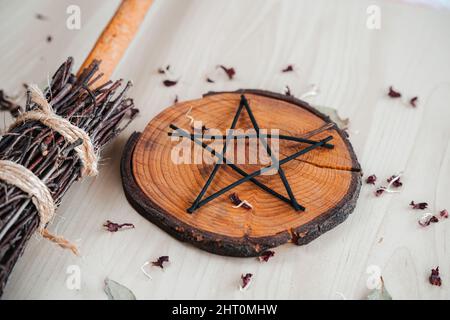 Hand made DIY besom broom and black pentagram on a white wooden table. Witchy closeup of ritual witchcraft items Stock Photo