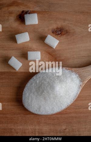Granulated sugar and sugar cubes in wooden spoon on wooden background Stock Photo