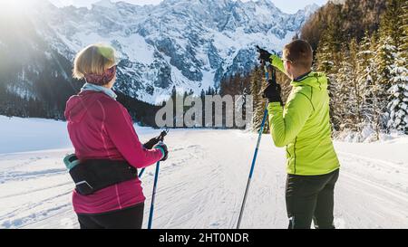 Senior couple, cross country skiers relaxing in the sun, looking at the mountain landscape, and skiing over the trail. Stock Photo