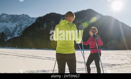 Caucasian cross country ski couple taking a break, talking and enjoying in beautiful snowy mountains nature, on a clear sunny winter day. Stock Photo