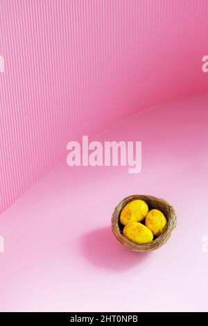 Easter eggs in a natural nest. Painted yellow-golden eggs on a pink background. Easter minimalistic concept. Copy space Stock Photo