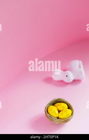 Easter eggs and rabbit on a pink background. Yellow-golden eggs in a nest. Easter concept. Copy space Stock Photo