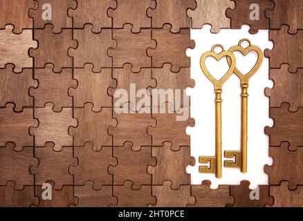 Two retro style bronze toned heart shaped keys on a wooden jigsaw puzzle background. Stock Photo