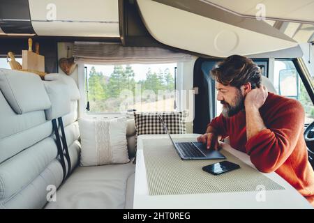 Young modern adult man work on laptop computer in remote working and digital job lifestyle inside a modern and connected camper van with nature woods Stock Photo
