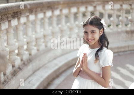 portrait of girl in communion dress with hands in prayer pose looking at camera with copy space Stock Photo