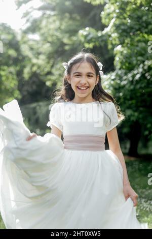 happy brunette girl in front in communion dress in a park Stock Photo