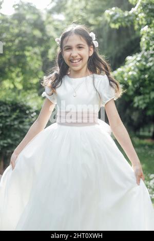 very happy girl showing her communion dress in a park Stock Photo