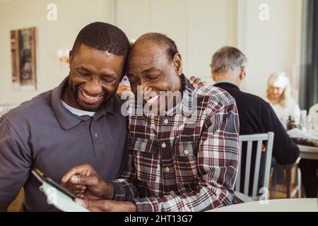 Cheerful senior man sharing smart phone with male nurse at retirement home Stock Photo