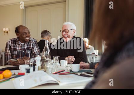 Cheerful elderly male friends talking at table in retirement home Stock Photo