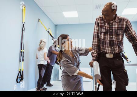 Smiling female caregiver helping senior man to walk at nursing home Stock Photo