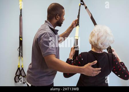 Male caregiver helping senior stretching resistance band in nursing home Stock Photo