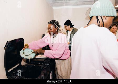 Young woman scraping leftovers in garbage bin while friends in kitchen at college dorm Stock Photo