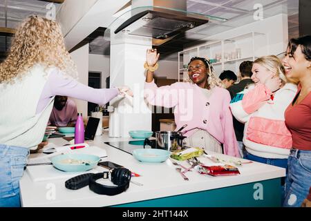 Happy multiracial young male and female friends having noodles in college dorm Stock Photo