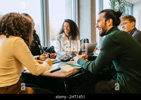 Cheerful students talking while sitting at table in cafeteria Stock Photo