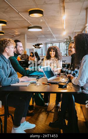 Smiling students talking while sitting at table in cafeteria Stock Photo