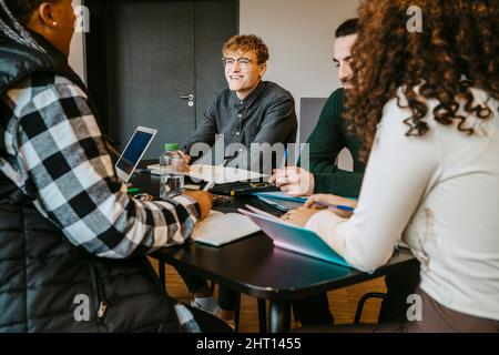 Smiling multiracial adult students studying together at table in cafeteria Stock Photo