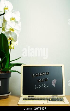 vertical photo with message of peace and love. In the composition there are a white orchid and work station with desk. Stock Photo
