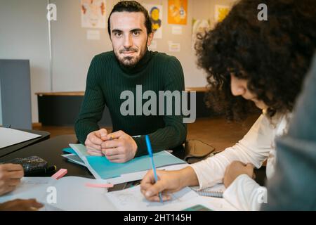 Portrait of confident young man sitting with female friend at table in university cafeteria Stock Photo