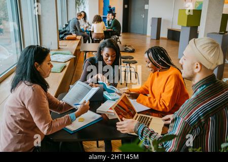 Smiling female students studying together with friends sitting table in university cafeteria Stock Photo