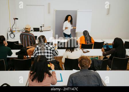 Smiling professor teaching students while standing by flipchart in classroom Stock Photo