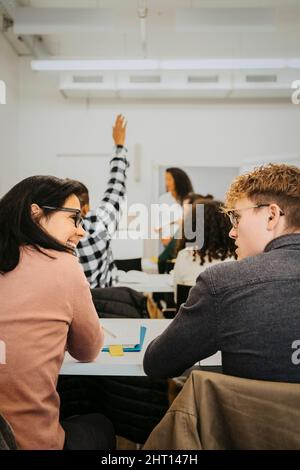 Rear view of male and female students talking while sitting together in classroom Stock Photo