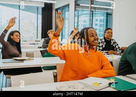 Female students raising hands while sitting in classroom Stock Photo