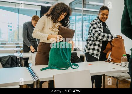Multiracial students packing backpack in classroom at community college Stock Photo