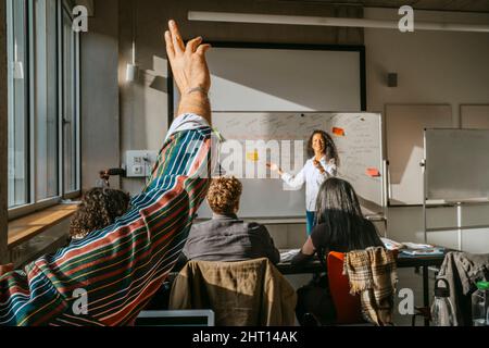 Cropped raised hand of male student with friends and teacher in classroom Stock Photo