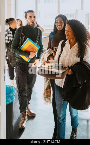 Smiling teacher walking with students in classroom at university Stock Photo