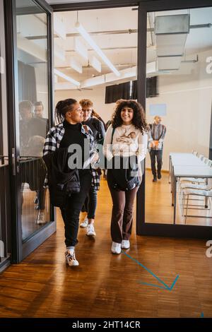 Smiling students leaving classroom while walking together Stock Photo