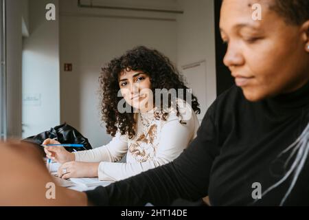 Portrait of woman with curly hair sitting by female friend in university Stock Photo