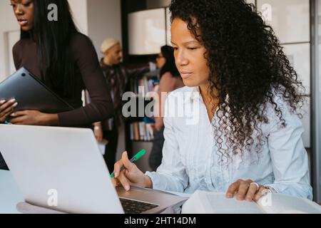 Confident female student using laptop while studying at community college Stock Photo