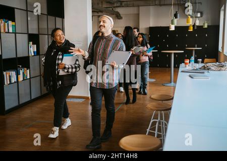 Cheerful friends talking while walking in front of students at university Stock Photo