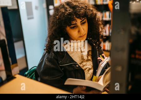 Young female student reading book in college library Stock Photo