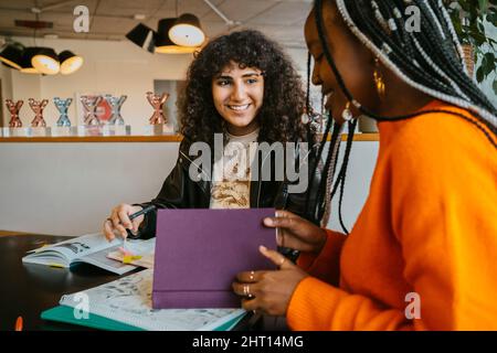 Smiling young woman looking at friend while studying together in university cafeteria Stock Photo