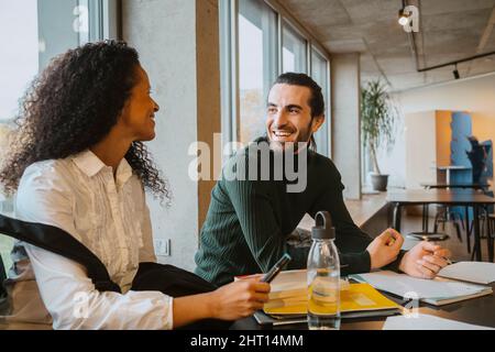 Smiling young man looking at female friend while studying together in college cafeteria Stock Photo