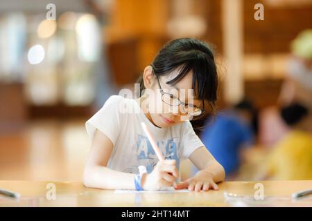 Girl with glasses concentrating on studying in creative education class Stock Photo