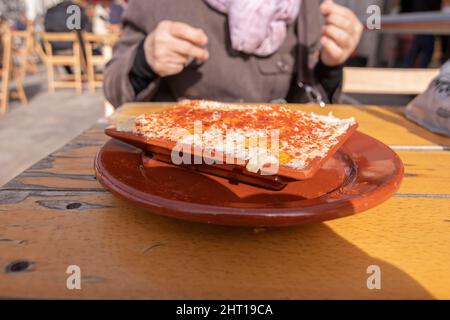Octopus salad, served in a clay dish. On a wooden table, outside, behind an unfocused woman. Spanish cuisine concept. Stock Photo