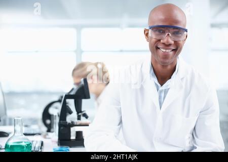 Smiling researcher. Portrait of a smiling young chemist in the lab with a female coworker in the background. Stock Photo